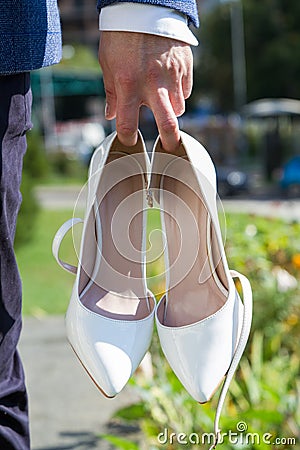 Shoes of the bride in the hands of the groom Stock Photo