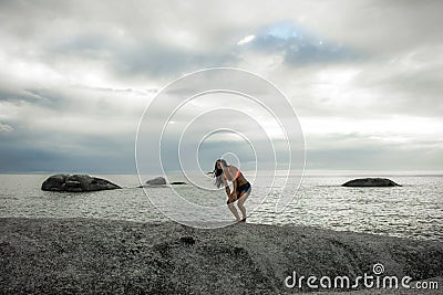 Woman laughing on a rock at sunset on Bakovern Beach, Cape Town. Stock Photo