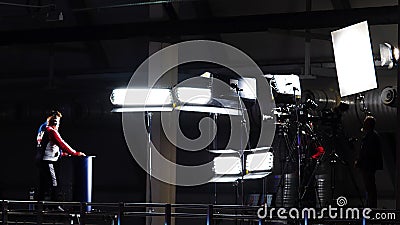 Shooting shows with professional light and camera. Stock footage. Presenters stand behind counter in front of camera and Editorial Stock Photo