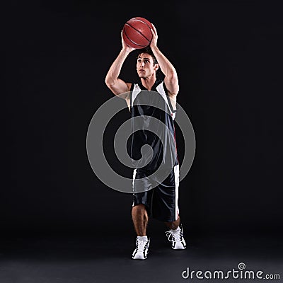 He shoots... he scores. Full length studio shot of a male basketball player ready to take a shot against a black Stock Photo