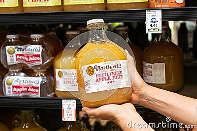 Shoppers hand holding a glass bottle of Martinelli`s brand 100% unfiltered apple juice Editorial Stock Photo