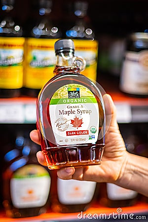 Shoppers hand holding a plastic bear jar of 365 whole foods brand of organic Grade A Maple syrup Editorial Stock Photo