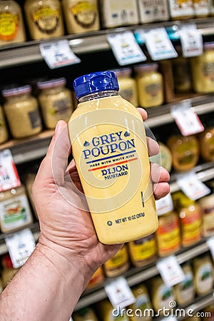 Shoppers hand holding a plastic container of grey poupon brand dijon mustard Editorial Stock Photo