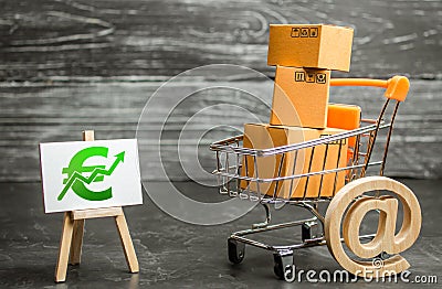 A shopping cart with boxes symbolizing internet trading and a stand with a green Euro up arrow. shopping online. sales of goods Stock Photo