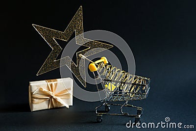 Shopping cart with a gold transparent star with sequins in the shape of a Christmas tree on a black background. Black Friday, buyi Stock Photo