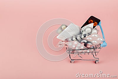 Shopping cart loaded with pills on a pink background. The concept of medicine and the sale of drugs. Copy space Stock Photo