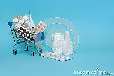 Shopping cart with medicinal pills and thermometer. Spray, vitamins, bottle lying near mini basket on blue background. Pharmacy Stock Photo