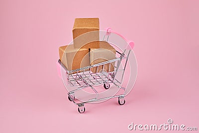 Shopping cart with package boxes on pink background. Shopping and delivering concept. Shop trolley full of parcels Stock Photo