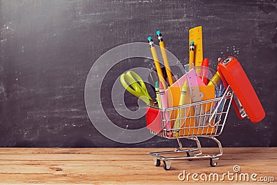 Shopping cart with school supplies over chalkboard background. Back to school sale concept Stock Photo