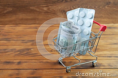Shopping cart with tablet blisters and dollar banknote. Spending money on pills and expensiveness of medicine concept. Stock Photo