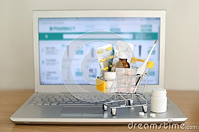 Shopping cart toy with medicaments in front of laptop screen with pharmacy web site on it. Pills, blister packs, medical bottles, Stock Photo