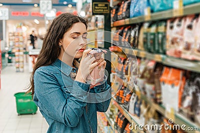 Shopping at the grocery store. A young brunette woman chooses a product by sniffing the fragrance through the packaging. Close up Stock Photo