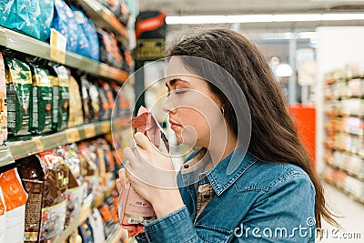 Shopping at the grocery store. A young brunette woman chooses a product by sniffing the fragrance through the packaging. Close up Stock Photo