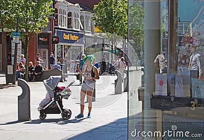 Shops on chapel street merseyside with people walking in the pedestrian ara and a young mother with green hair with a baby in a Editorial Stock Photo