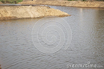 The shore of an artificial pond. A mound of sand on the water. Stock Photo