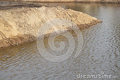 The shore of an artificial pond. A mound of sand on the water. Stock Photo
