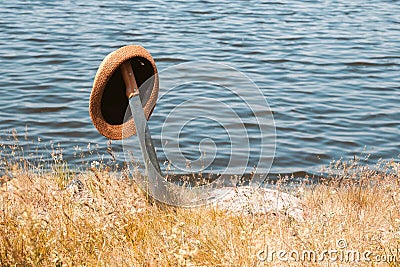 On the shore of the pond stuck in the ground sword on it hangs a hat with a brim summer day bright sun Stock Photo