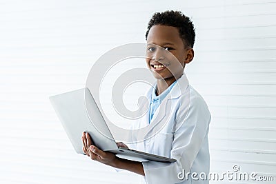 Short haired african american boy in white lab coat holding computer laptop in both hands. He smiled happily as he prepared and Stock Photo