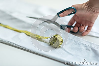 Shortening jeans. White jeans, Measuring tape, scissors on table. Jeans cutting. Stock Photo