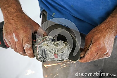 Shortening screw with old rotary cutter, sparks flying as metal is cut, closeup detail on man unprotected hands holding the piece Stock Photo