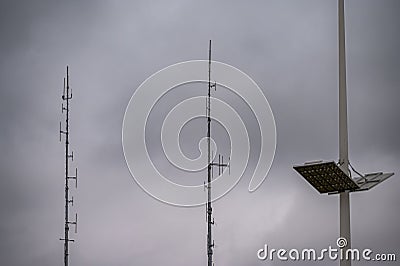 Shortwave antennas and outdoor LED panel light on big masts against gray clouds Stock Photo