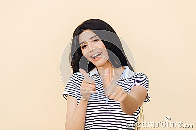 Shot of attractive European female gives double thumb up, has positive expression, has white teeth with brackets, dressed casually Stock Photo