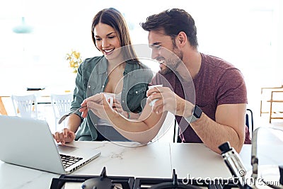 Beautiful lovely young couple using their laptop and having breakfast in the kitchen at home Stock Photo