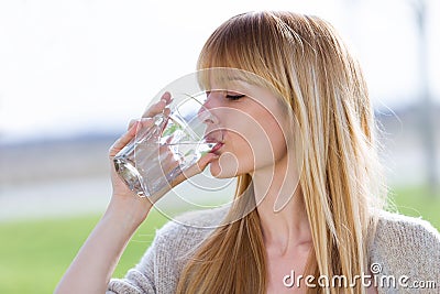 Beautiful young woman drinking water glass in the park. Stock Photo