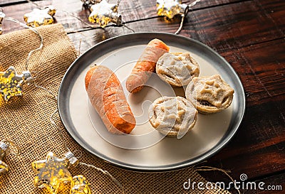 Shot of carrots and mince pies on a dish, festive star-shaped Christmas lights in the background Stock Photo