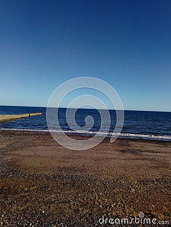 A shot of a clear summers sky over a deep blue ocean lapping ashore a pebbley beach, Dawlish, Devon, UK Stock Photo
