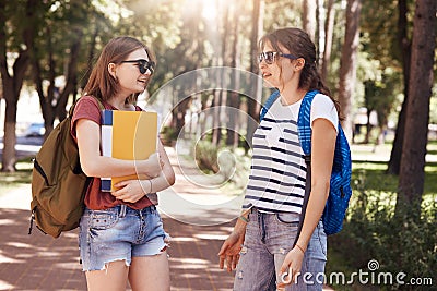 Shot of college students meet accidentally in park, carry bags and books, have pleasant talk , chat about latest news at universit Stock Photo