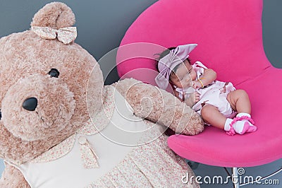 A shot of a cute baby girl with purple headband and big teddy bear while sleeping and playing on the pink chair / Focus at infant Stock Photo