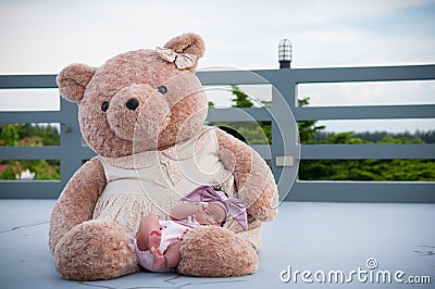 A shot of a cute baby girl with purple headband while sleeping and playing with big teddy bear on the rooftop / Focus at infant g Stock Photo