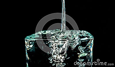 Fresh water pouring into a glass, overflowing and flying to the sides Stock Photo