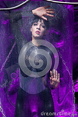 Shot of a futuristic young person posing near glass space capsule with wires and purple neon light on black background Stock Photo