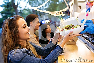 Group of attractive young friends choosing and buying different types of fast food in eat market in the street. Stock Photo