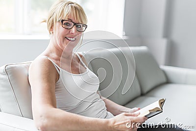 Shot of a mature woman reading her favorite novel while at home in living room. Stock Photo