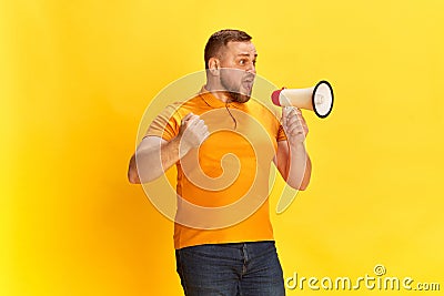 Shot of one bearded man holding megaphone and shouting over yellow background Stock Photo