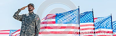 Shot of patriotic soldier in military uniform giving salute near american flags with stars and stripes Stock Photo