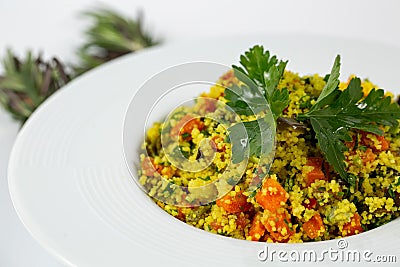 Shot of a a plate of Couscous with vegetables on a white table decorated with green plants Stock Photo