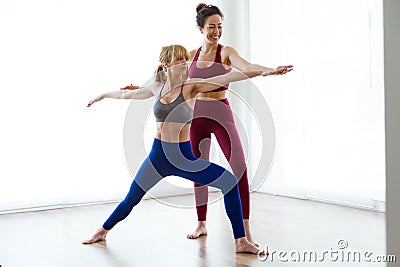 Pretty young yoga instructor helping her student in a yoga session at home. Virabhadrasana II pose. Stock Photo