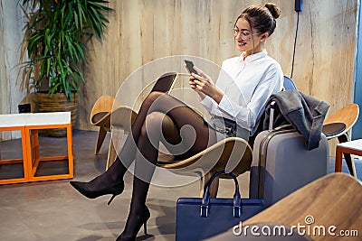 Smart young businesswoman texting with her mobile phone sitting in the hotel lobby Stock Photo
