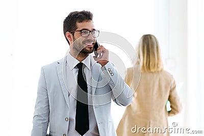 Smiling young businessman talking with his smartphones in a hallway of they company. Stock Photo