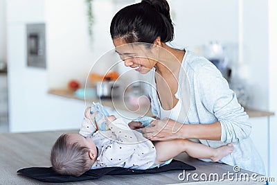 Smiling young mother has fun with little baby while changing his nappy at home Stock Photo