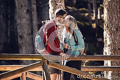 Two travel hikers with backpack kissing while standing on the wood bridge in the forest Stock Photo