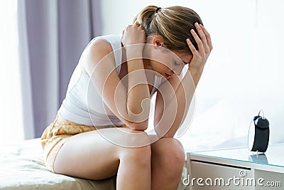 Unhappy lonely depressed young woman sitting on bed at home. Depression concept. Stock Photo