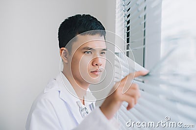 Shot of a young male doctor standing in doctor`s room and looking through the window Stock Photo