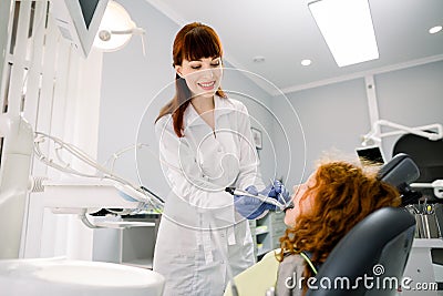 Shot of young pretty female Caucasian dentist in white uniform, making dental check up and caries treatment with drill Stock Photo