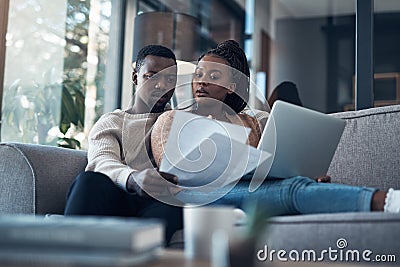 Should we reinvest this money. a young couple sitting on the sofa together and using a laptop while going through their Stock Photo