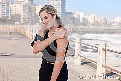 Shoulder pain, fitness woman and music of a person running by the sea with a arm injury. Workout, sports and training Stock Photo